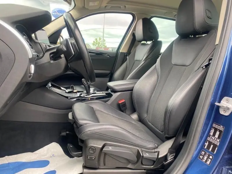 Vue intérieure côté conducteur d’un BMW X3 X-DRIVE 20 DA bleu métal 2018, sièges cuir noirs et console centrale visible.