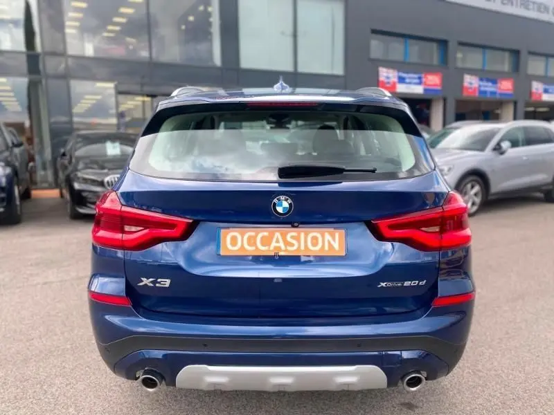 Vue arrière d’un BMW X3 bleu métal X-Drive 20 DA 190 CV avec logo et feux rouges distinctifs, en concession.