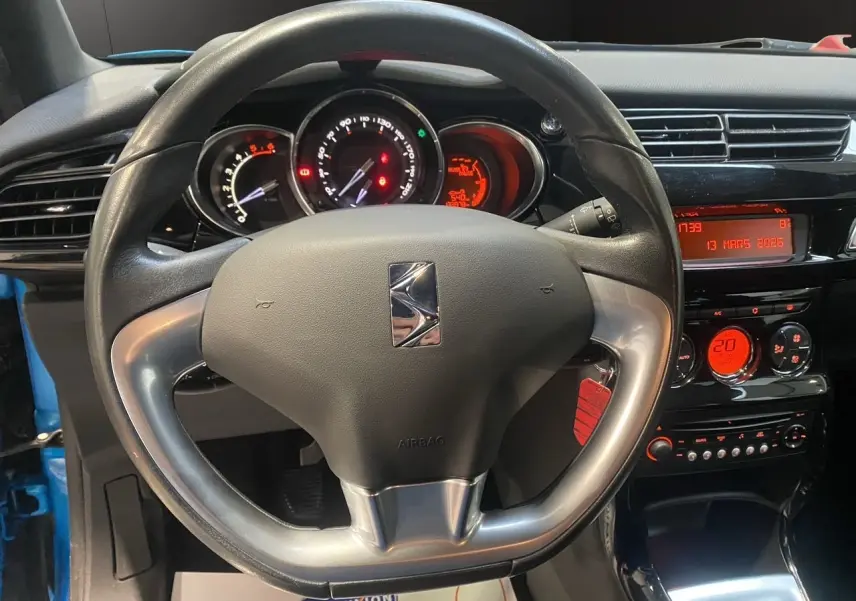 Vue intérieure centrée sur le volant et le tableau de bord noir du Citroën DS3, avec affichages numériques rouges.