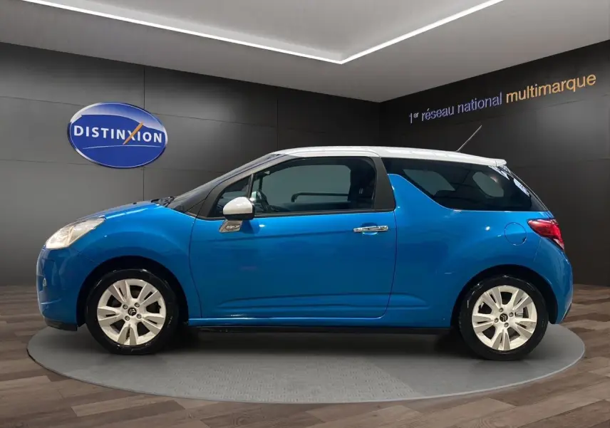 Profil droit d'une Citroën DS3 bleu avec toit blanc, en intérieur sur un plateau rotatif, mettant en valeur ses jantes blanches.