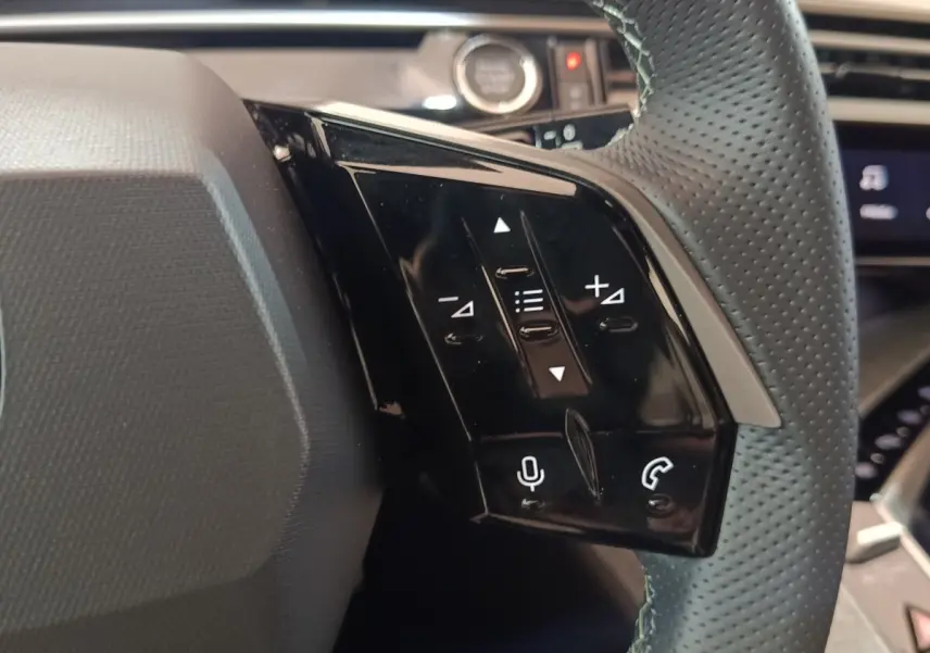 Gros plan sur les commandes noires du volant cuir perforé du Peugeot 5008 gris clair, version hybride rechargeable 2026.