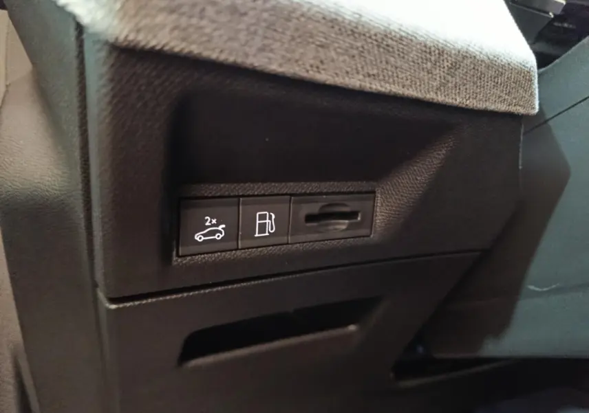 Détail des commandes d'ouverture du coffre et de la trappe à carburant sur le tableau de bord noir du Peugeot 5008 gris clair.