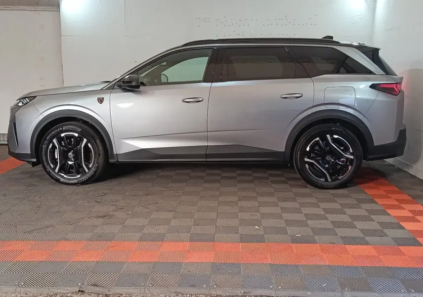 Vue de profil côté gauche d'un Peugeot 5008 gris clair avec jantes noires et toit noir dans un garage.
