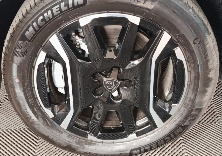 Gros plan sur la jante noire et argentée avec logo Peugeot, montée d’un pneu Michelin sur Peugeot 5008 gris clair.