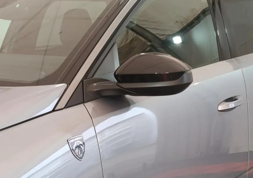 Gros plan sur le côté gauche gris clair du Peugeot 5008 2026, avec rétroviseur noir et logo Peugeot visible.