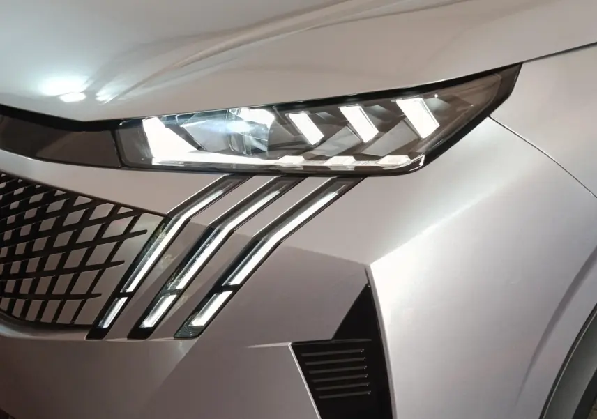 Gros plan sur le phare avant droit et la calandre en losange du Peugeot 5008 gris clair, version 2026.