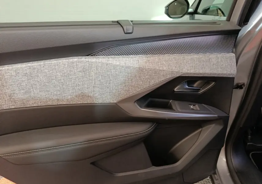 Gros plan sur la porte intérieure côté droit du Peugeot 5008 gris clair, avec habillage tissu gris et commandes de fenêtre.