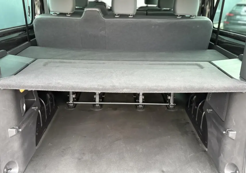 Coffre spacieux vu de l'arrière dans un Nissan Primastar Combi noir métallisé avec banquette arrière et cache-bagages.