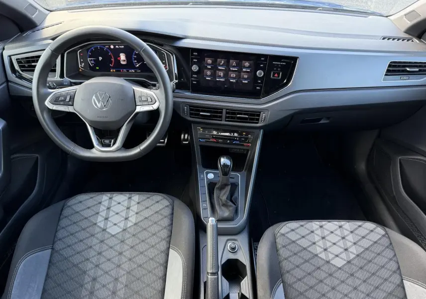 Vue intérieure frontale du tableau de bord et volant cuir multifonctions du Volkswagen Taigo 2025 avec console centrale et sièges tissu noir à motifs.