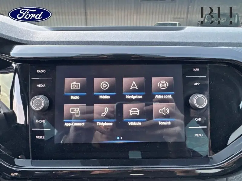 Écran tactile central du tableau de bord d'un Volkswagen T-Cross noir, affichant les menus multimédias et navigation.