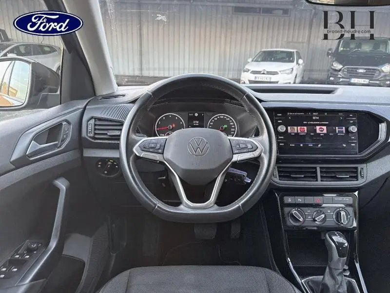 Vue frontale de l'intérieur du Volkswagen T-Cross noir, volant cuir multifonction et écran tactile central visible.