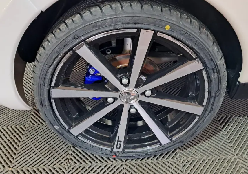 Gros plan sur la roue avant droite de l'AIXAM AMBITION 0.5 CITY COUPE GTI blanche avec jante noire et logo GTI.