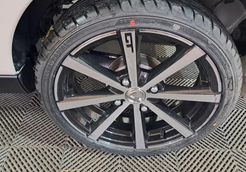 Gros plan sur la jante noire et grise avec logo GT de l'AIXAM AMBITION 0.5 CITY COUPE GTI blanche, côté roue avant.