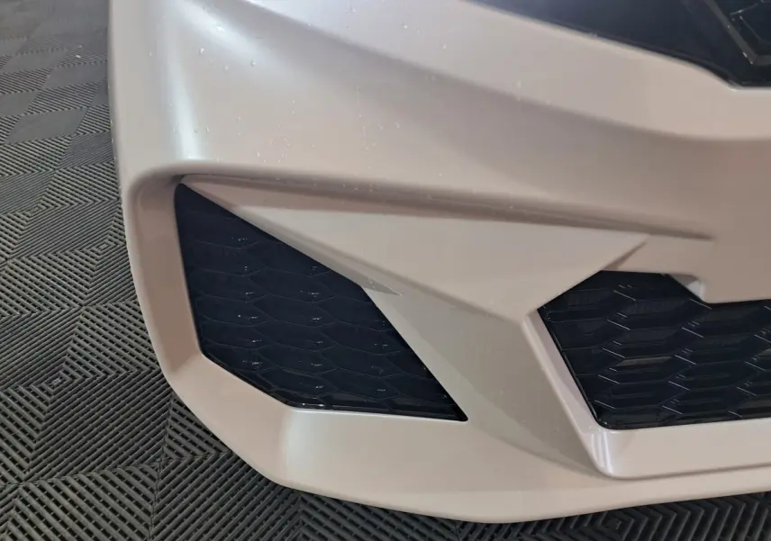 Gros plan sur la partie avant gauche blanche de l'AIXAM AMBITION 0.5 CITY COUPE GTI avec grille noire texturée.