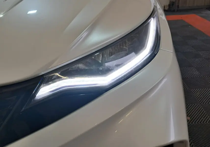 Gros plan sur le phare avant droit blanc d'une Aixam Ambition 0.5 City Coupe GTI 2026 avec éclairage LED allumé.