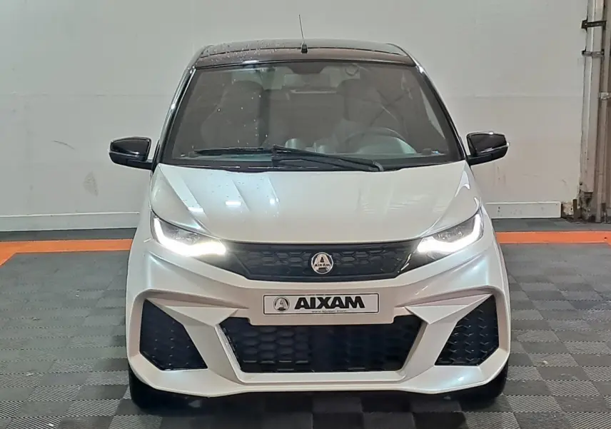 Vue de face d'une Aixam Ambition 0.5 City Coupe GTI blanche avec phares allumés et rétroviseurs noirs.