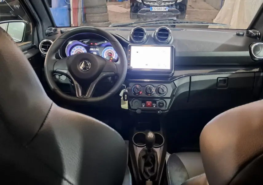 Vue intérieure avant de l'AIXAM Ambition 0.5 City Coupe GTI 2026, tableau de bord noir avec écran tactile central lumineux.