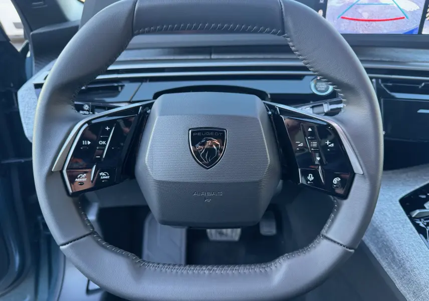 Vue rapprochée du volant cuir noir du Peugeot 3008 Hybrid 2025 avec commandes intégrées et écran de recul visible.