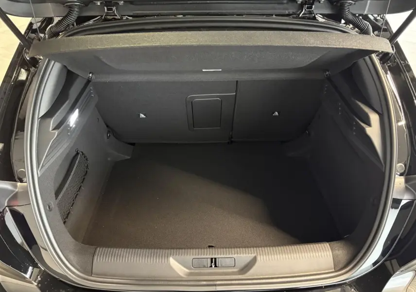 Coffre ouvert vu de dessus d'une Peugeot 308 noire métallisée, montrant l'espace de rangement et la moquette noire.