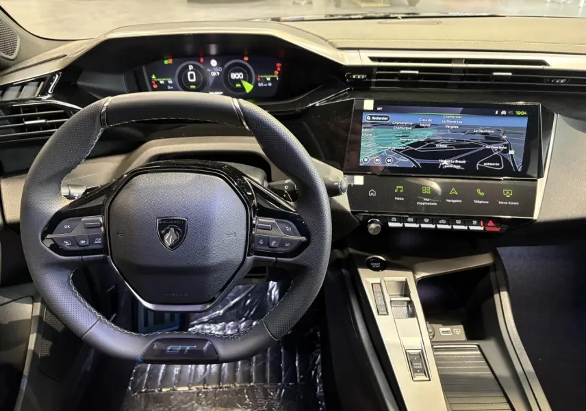 Vue intérieure centrée sur le volant GT cuir noir avec surpiqûres vert Adamite et écran tactile de navigation Peugeot 308 2026.