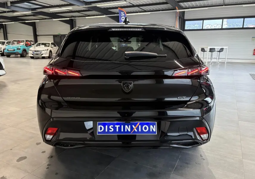Vue arrière d’une Peugeot 308 GT noire métallisée avec feux arrière LED en forme de griffes, en showroom.
