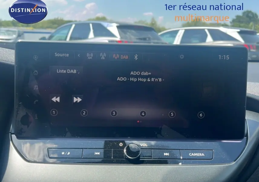 Écran tactile central du Nissan Juke hybride 2025 gris squale metal, affichant la radio DAB en extérieur lumineux.