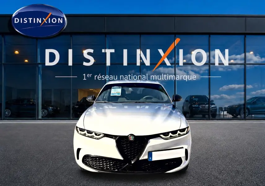 Vue frontale d'une Alfa Romeo Tonale blanche 2025 avec calandre noire et phares LED, devant une vitrine Distinxion.