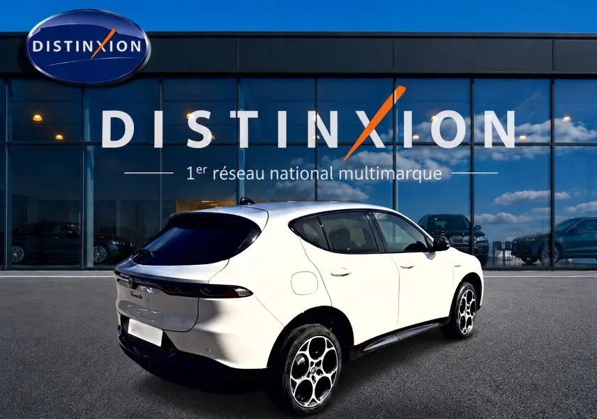 Vue 3/4 arrière droite d'un Alfa Romeo Tonale blanc avec jantes alu distinctives, stationné devant un showroom Distinxion.