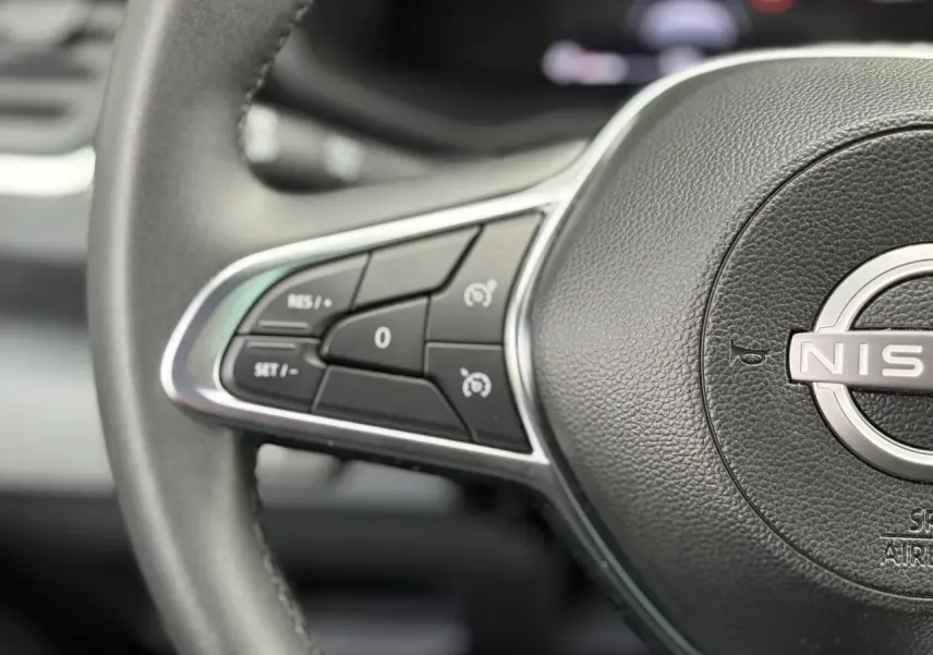 Gros plan sur les commandes au volant noir du Nissan Primastar Combi 2025, soulignant le logo central et les boutons de régulateur.