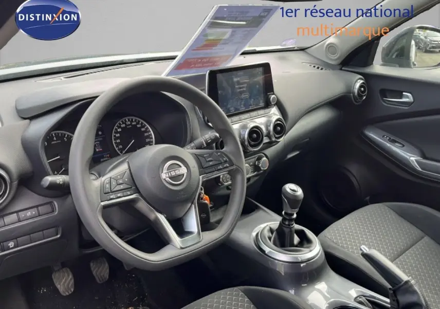 Vue intérieure côté conducteur du tableau de bord et volant du Nissan Juke 2023 en tissu noir avec écran tactile central.