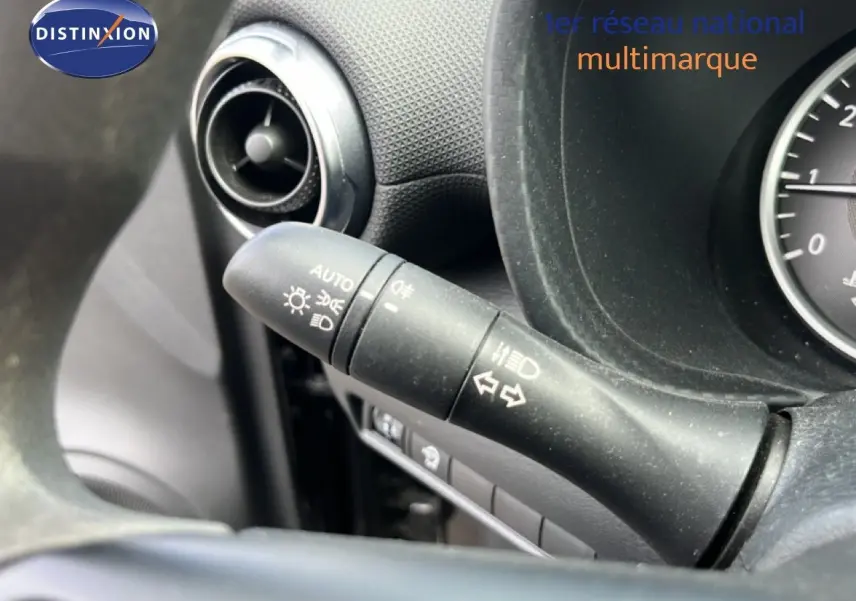 Gros plan sur le commodo d'éclairage à gauche du volant du Nissan Juke noir métal, tableau de bord partiel visible.