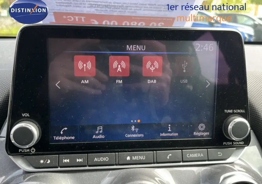 Vue intérieure centrée sur l'écran tactile multimédia du Nissan Juke noir métal 2023 avec commandes audio et caméra.