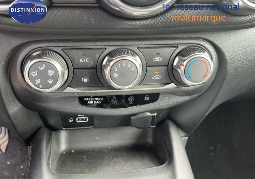 Vue rapprochée du tableau de bord du Nissan Juke noir métal 2023, montrant les commandes de climatisation et ports USB.