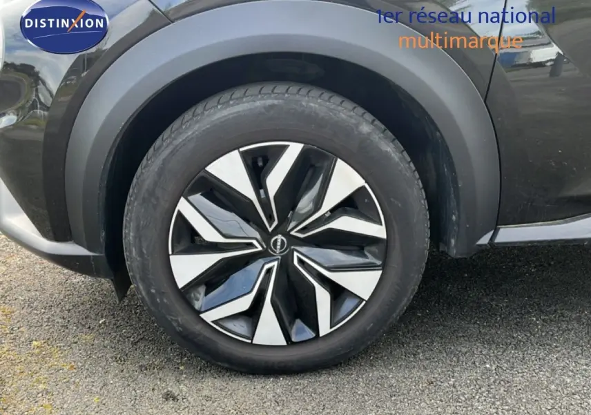 Gros plan sur la roue avant gauche du Nissan Juke noir métal 2023, mettant en valeur la jante au design moderne bicolore.