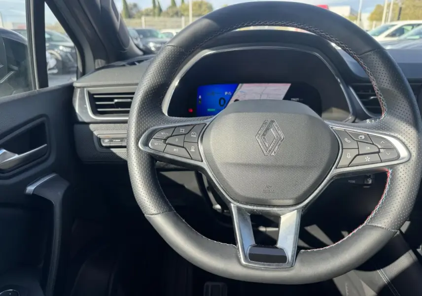 Vue intérieure centrée sur le volant noir perforé de la Renault SYMBIOZ E-Tech hybride avec tableau de bord numérique en arrière-plan.