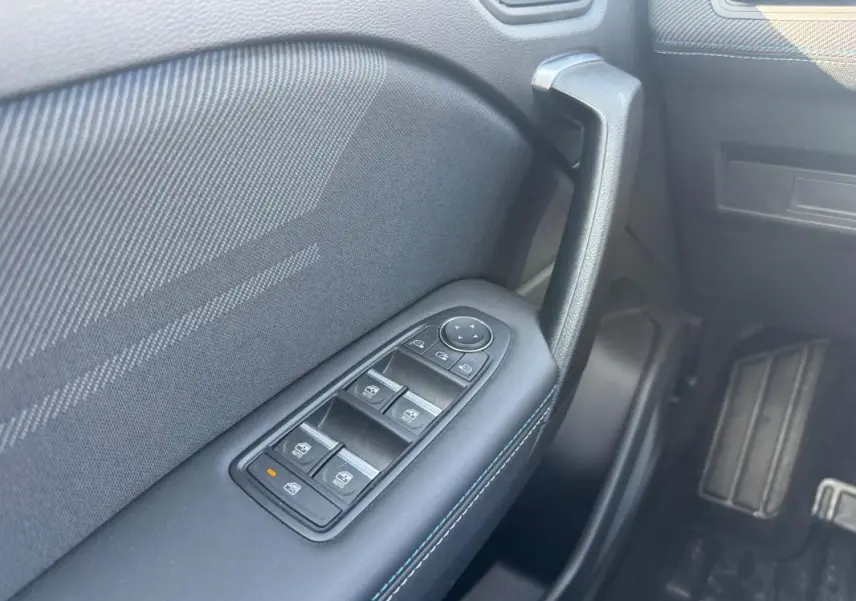 Gros plan sur la commande des vitres électriques côté gauche de la Renault SYMBIOZ gris clair, avec poignée de porte noire.