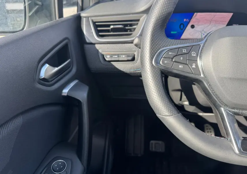 Vue intérieure côté gauche du volant perforé et du tableau de bord numérique bleu du Renault Symbioz gris clair.