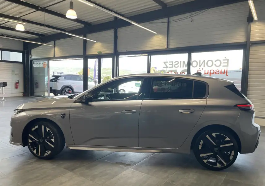 Peugeot 308 gris Artense vue de profil côté gauche en intérieur, jantes alliage bi-tons et blason sur aile avant.