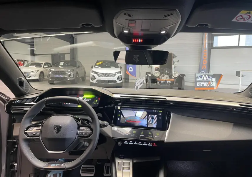 Vue intérieure avant de la Peugeot 308 GT 2026 gris Artense, avec tableau de bord numérique et écran tactile central allumé.
