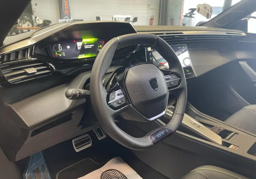 Vue intérieure du poste de conduite Peugeot 308 GT 2026, volant cuir noir avec logo GT et tableau de bord numérique.