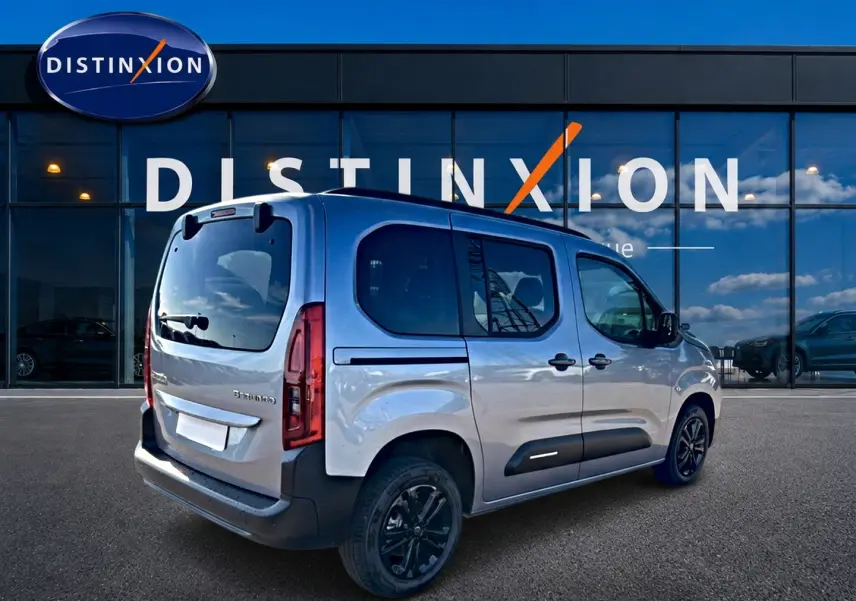 Vue 3/4 arrière droite du Citroën Berlingo Steel Grey avec barres de toit et jantes alu noires devant un showroom Distinxion.