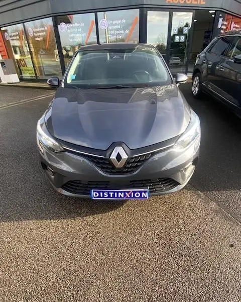 Vue avant d'une Renault Clio gris métallisé 2021, avec logo distinctif et plaque "DISTINXION" visible devant un bâtiment.