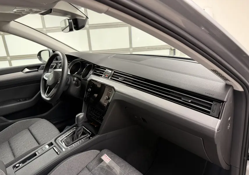 Vue intérieure côté conducteur de la Volkswagen Passat SW 2024 gris pyrite, avec tableau de bord moderne et boîte automatique.