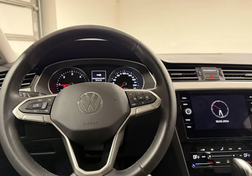 Vue intérieure centrée sur le volant noir de la Volkswagen Passat SW 2024 avec tableau de bord et écran tactile.
