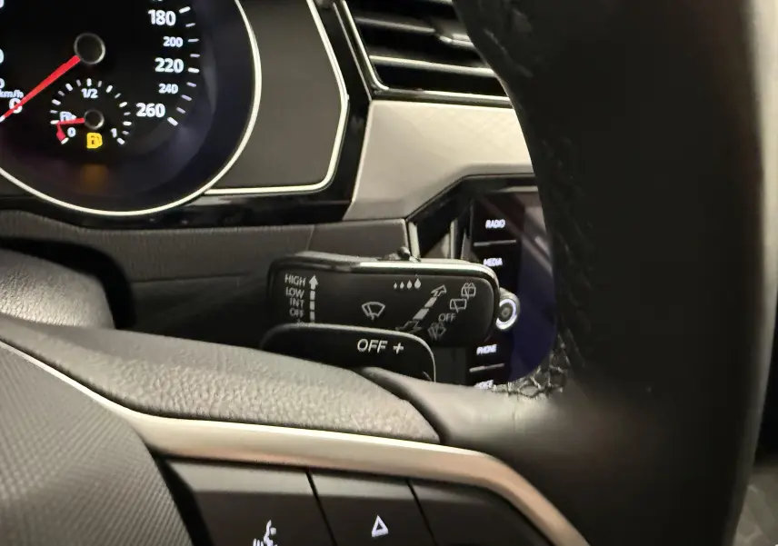 Gros plan sur la commande d’essuie-glace à gauche du volant dans l’habitacle gris et noir de la Volkswagen Passat SW 2024.
