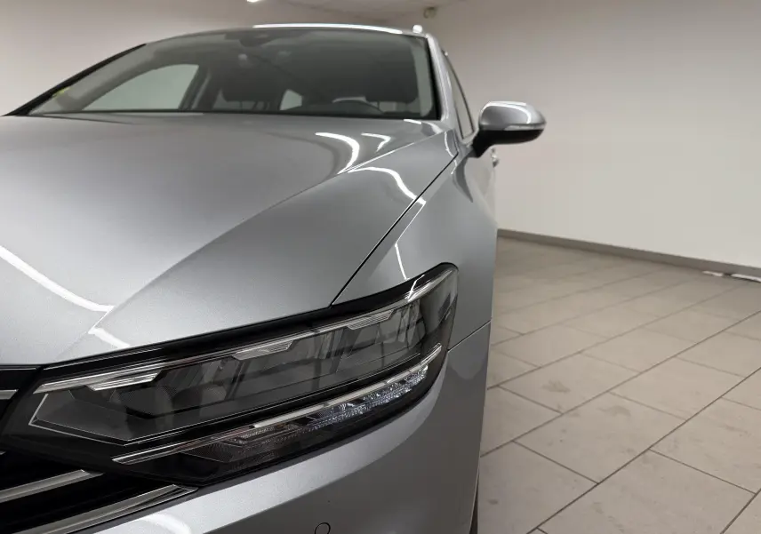 Vue rapprochée 3/4 avant droit de la Volkswagen Passat SW 2.0 TDI Business 2024 en gris pyrite métallisé avec phares LED.
