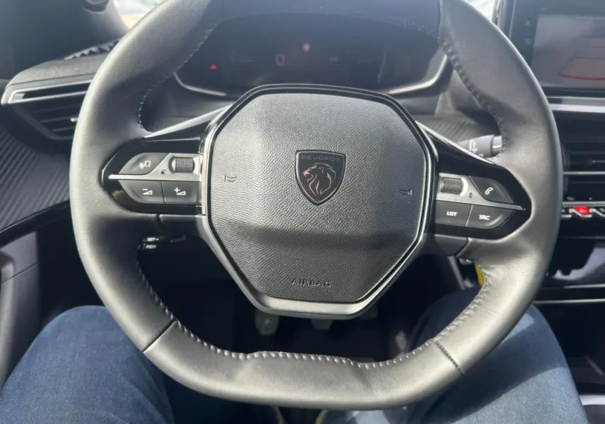 Vue rapprochée du volant cuir noir du Peugeot 2008 2024 avec commandes intégrées et logo central.