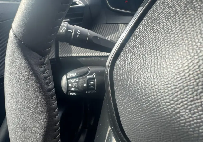 Gros plan sur la commande de régulateur de vitesse à gauche du volant en cuir noir du Peugeot 2008 blanc 2024.