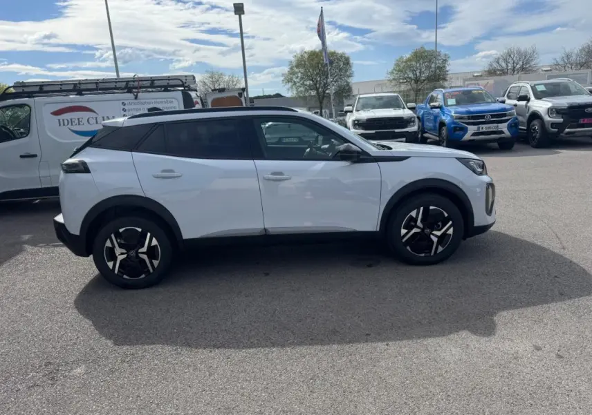 Peugeot 2008 blanc vue de profil côté gauche, avec jantes alliage 17 pouces et barres de toit noires.