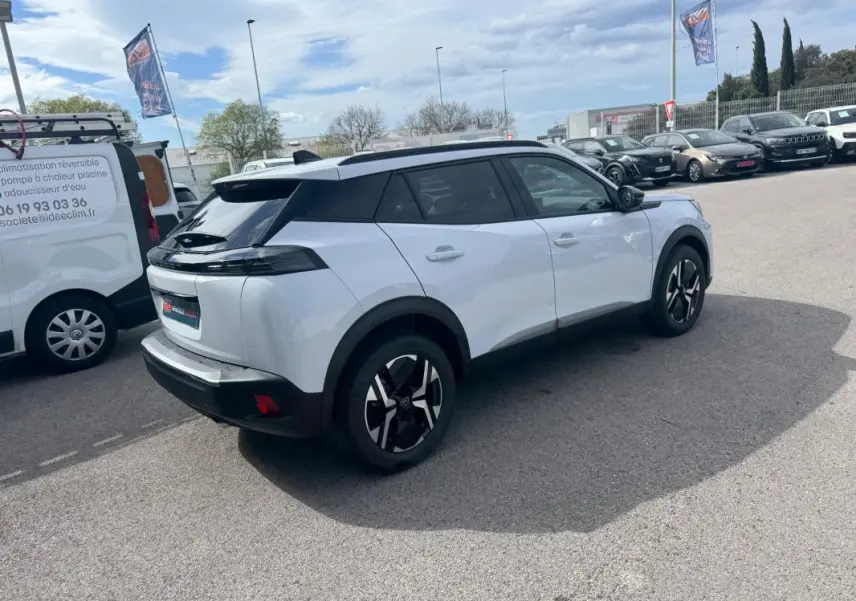 Peugeot 2008 blanc vue 3/4 arrière droit avec barres de toit et jantes alliage 17 pouces sur parking.